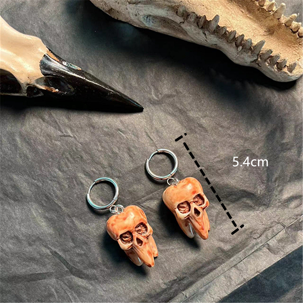Two small skull-shaped charms on a dark surface with a measurement label.