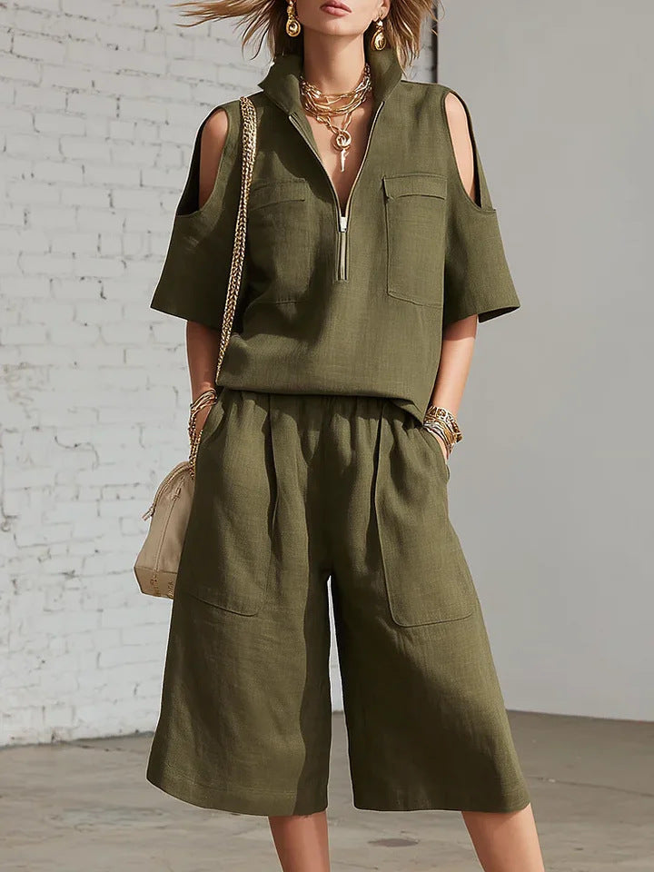 Person wearing an olive green outfit with a matching bag against a white brick wall.