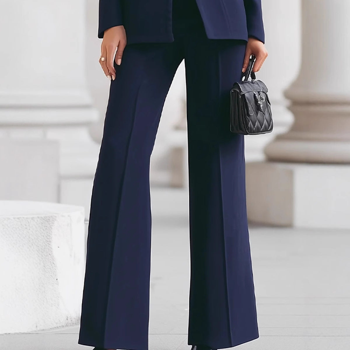 Person wearing a navy blue suit with wide-leg pants holding a black handbag.