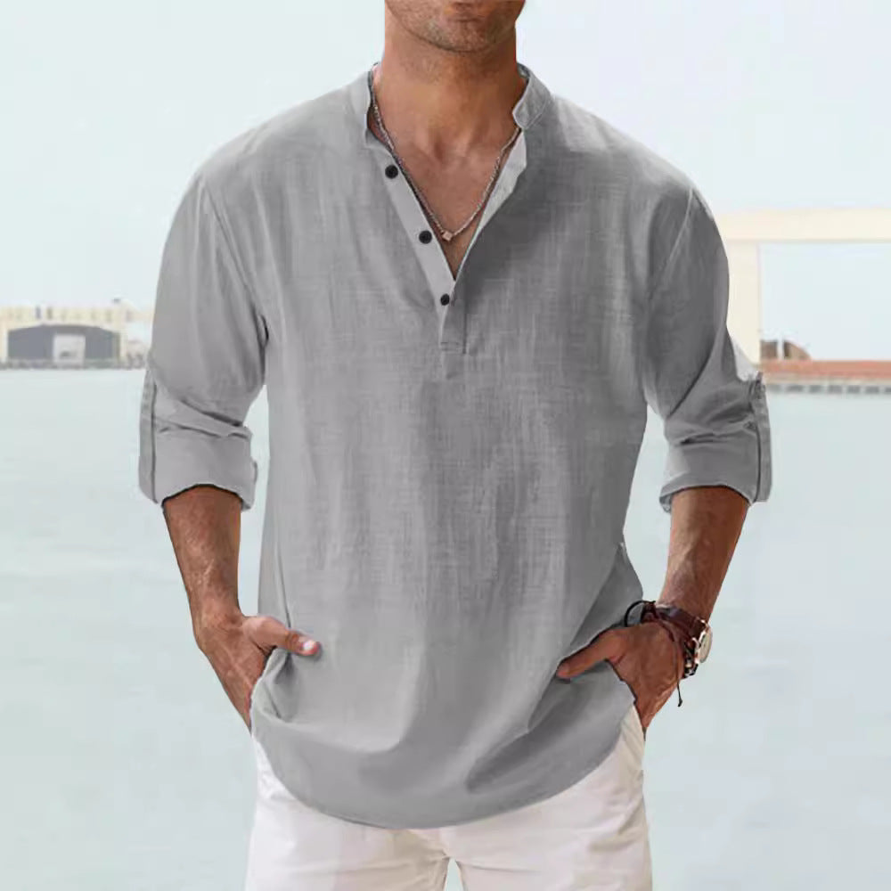 Man wearing a gray long-sleeve shirt with rolled-up sleeves against a blurred outdoor background