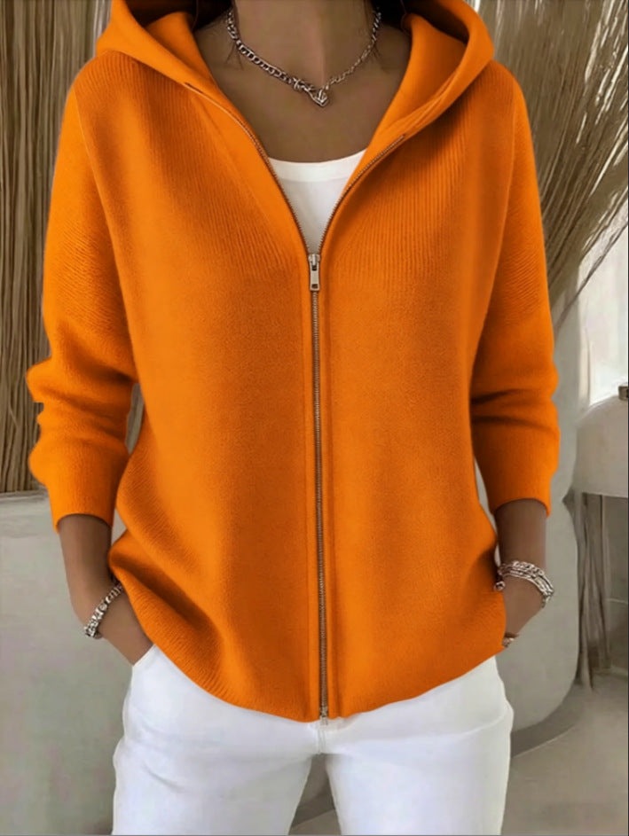 Person wearing an orange zip-up hoodie and white pants indoors.