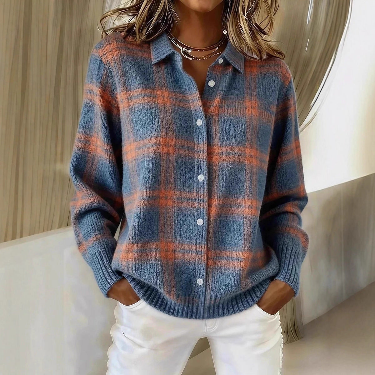 Person wearing a blue and orange plaid sweater with white pants indoors.