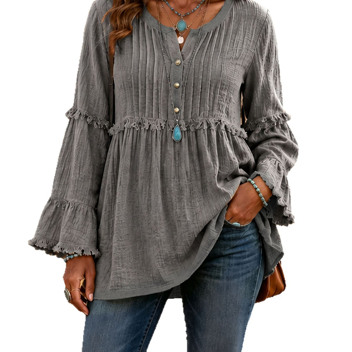 A woman wearing a gray long-sleeve blouse with a buttoned V-neck, gathered waist, and ruffled cuffs, paired with blue jeans against a plain white background.
