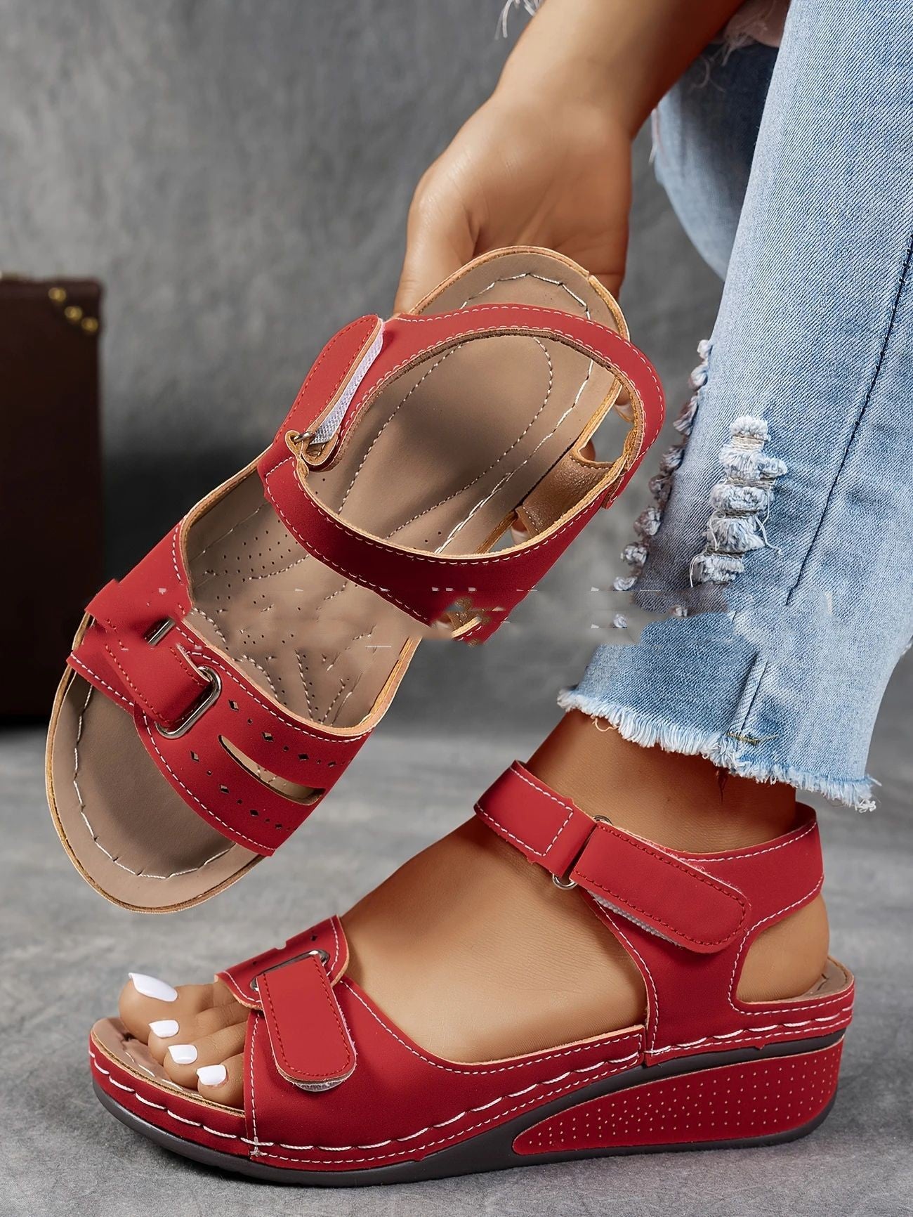 Red sandals worn with light blue jeans on a neutral background