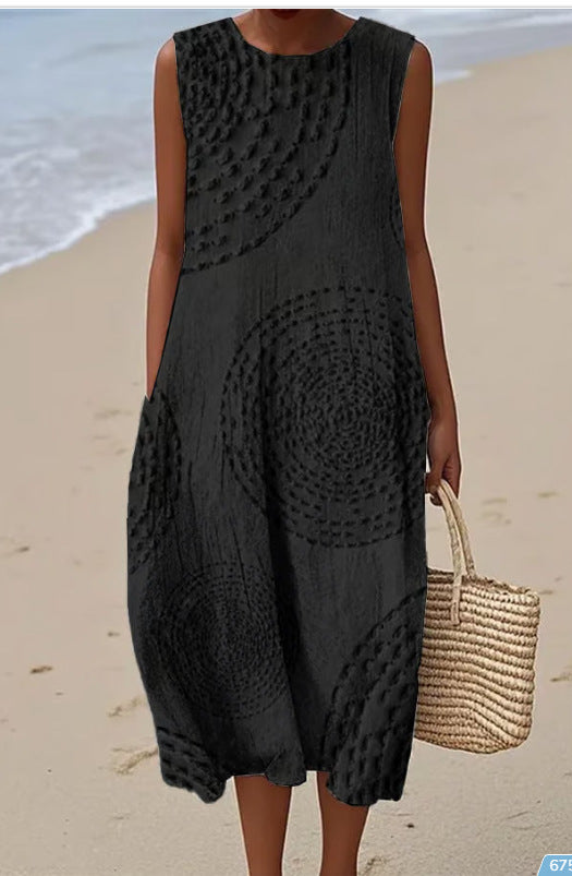 Person wearing a black sleeveless dress with circular patterns on a beach.