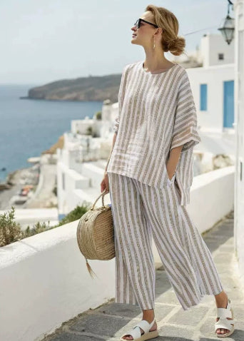 Woman in striped outfit with a straw bag standing on a Mediterranean street.