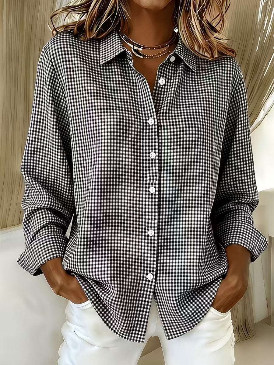 A woman wearing a black and white gingham check long-sleeve button-down shirt with white pants, standing indoors.