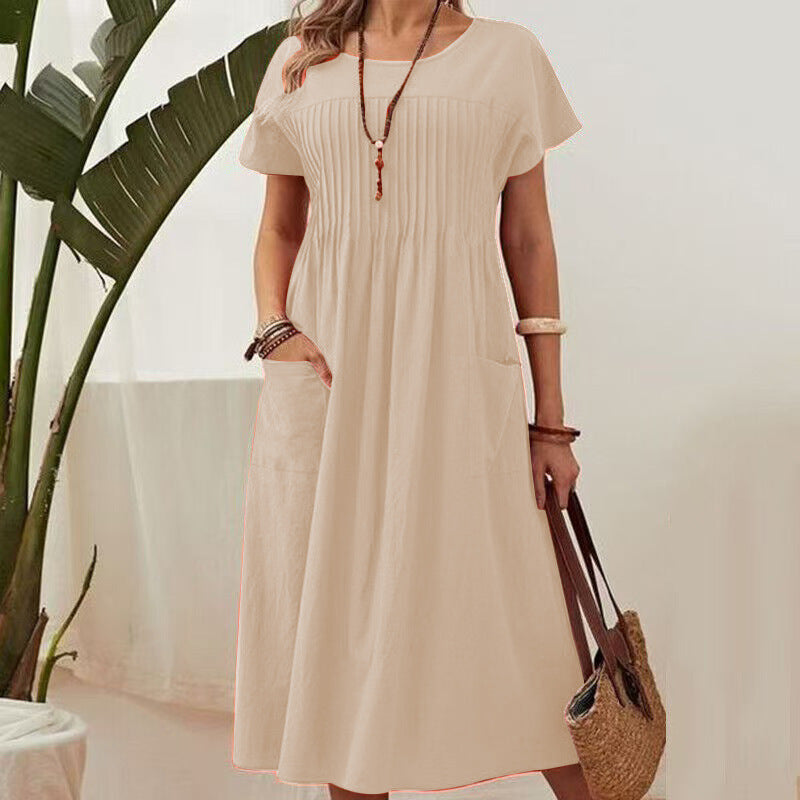 Woman wearing a beige dress holding a straw bag with a plant in the background