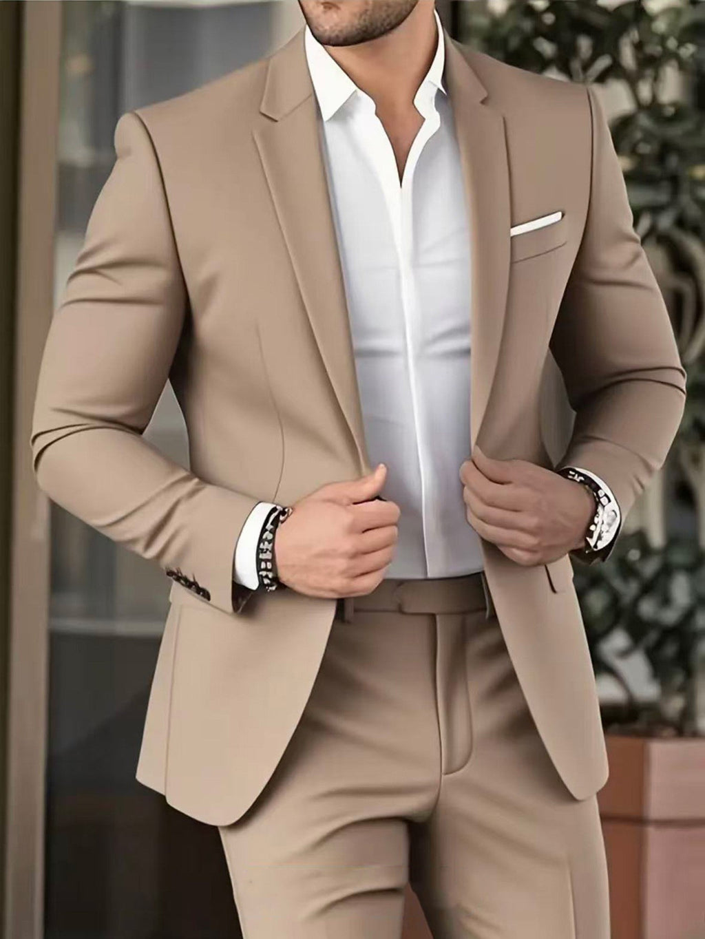 Man wearing a beige suit with a white shirt, standing outdoors.