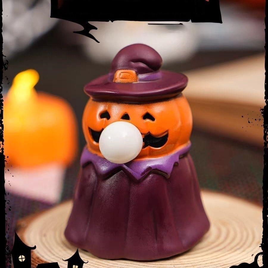 A Halloween-themed jack-o'-lantern candy holder shaped like a witch, featuring an orange pumpkin head with a white bubblegum bubble, a purple witch hat, and a purple robe, sitting on a wooden coaster.