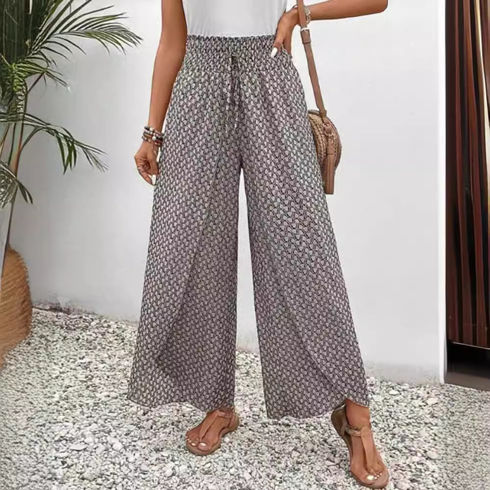 Person wearing patterned wide-leg pants standing indoors with a plant and curtain in the background.
