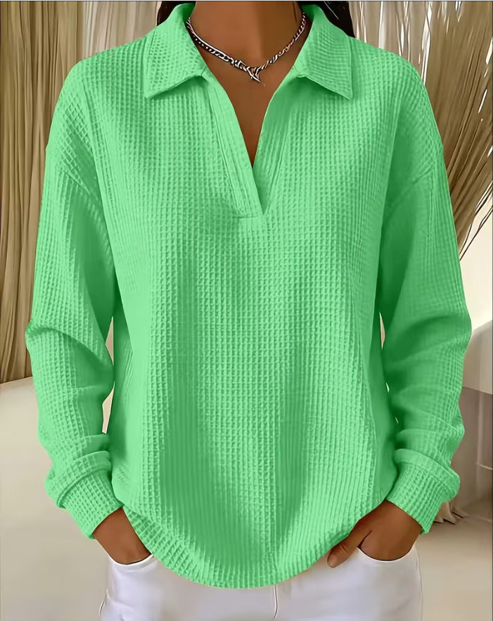 A woman wearing a bright mint green waffle-knit long-sleeve polo shirt with a split collar and split placket, paired with white pants and a silver necklace.
