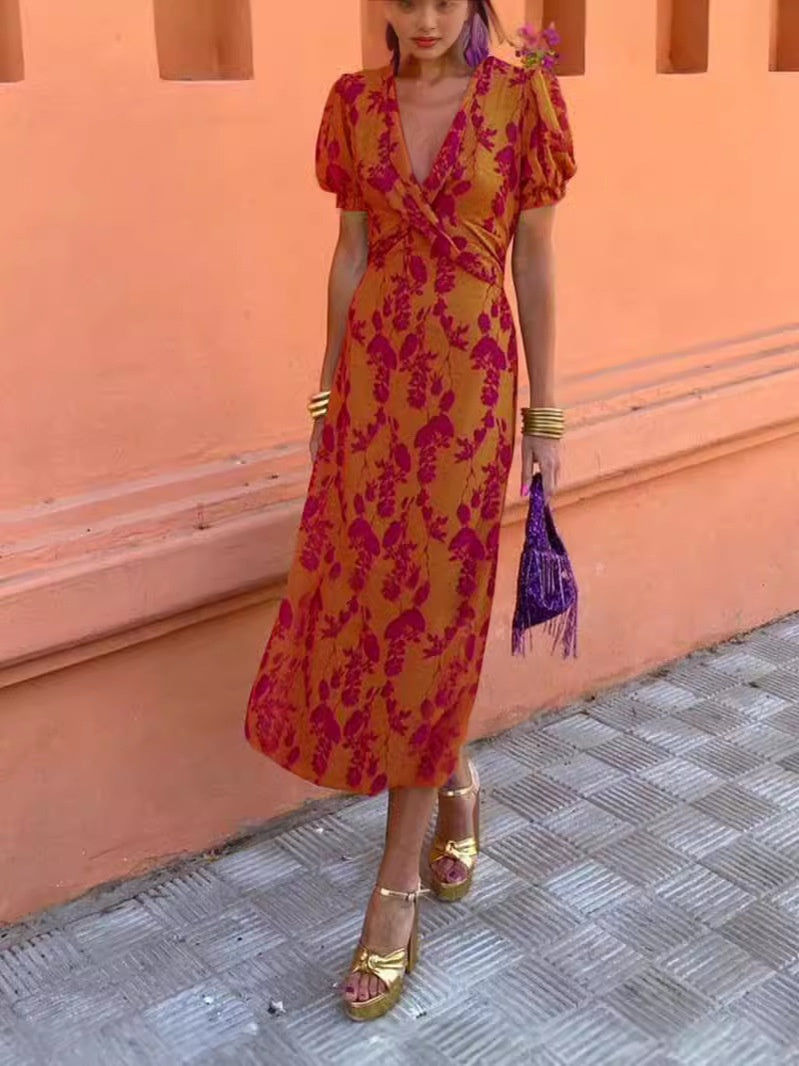 Woman in a floral dress standing against a peach-colored wall.