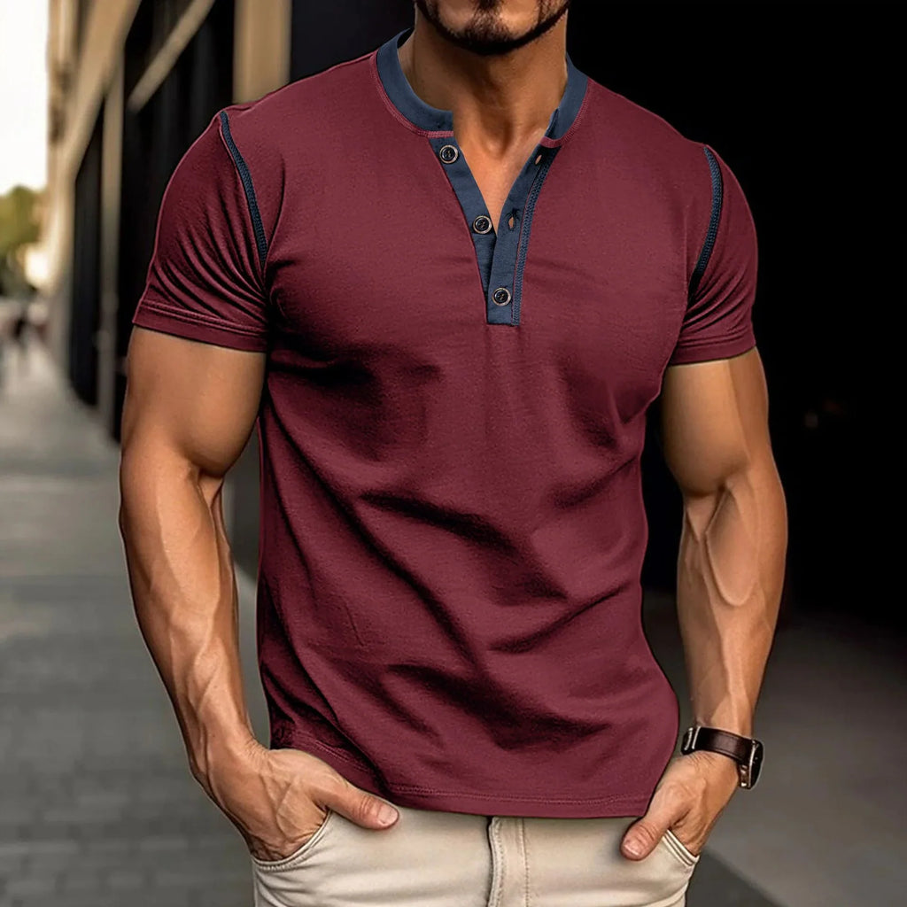 Man wearing a maroon henley shirt with blue accents on a blurred street background