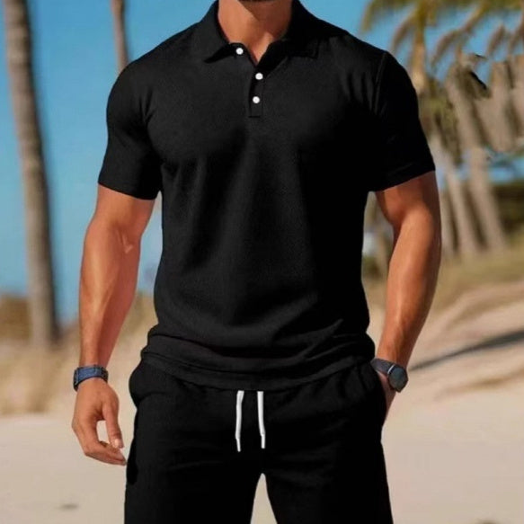 Man wearing a black polo shirt and black pants with white drawstring on a beach.