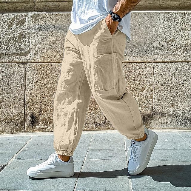 Person wearing beige cargo pants and white sneakers against a stone wall.