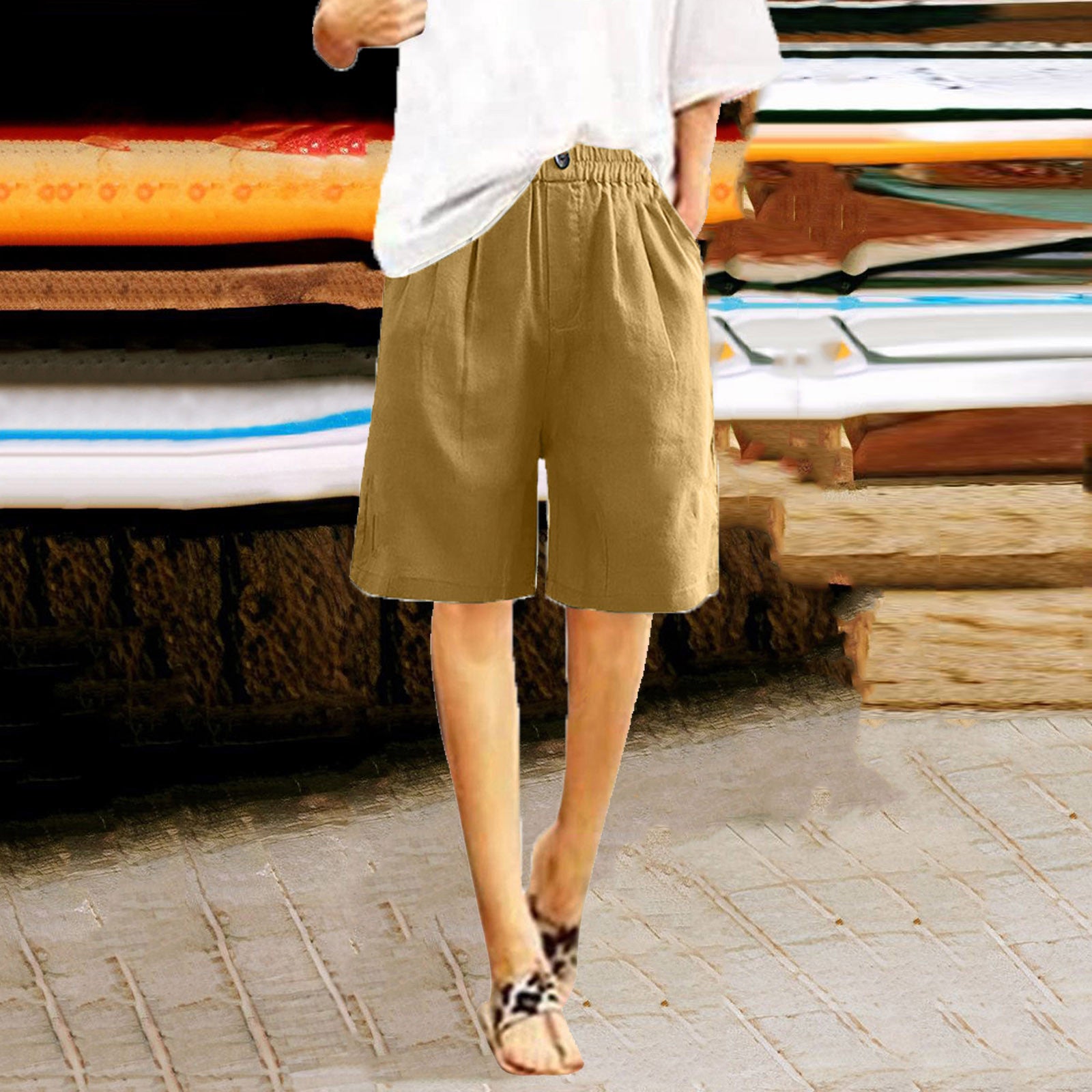 Person wearing beige shorts standing on a sidewalk with stacked surfboards in the background.