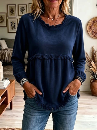 Woman wearing a navy blue top with ruffled details in a living room setting.
