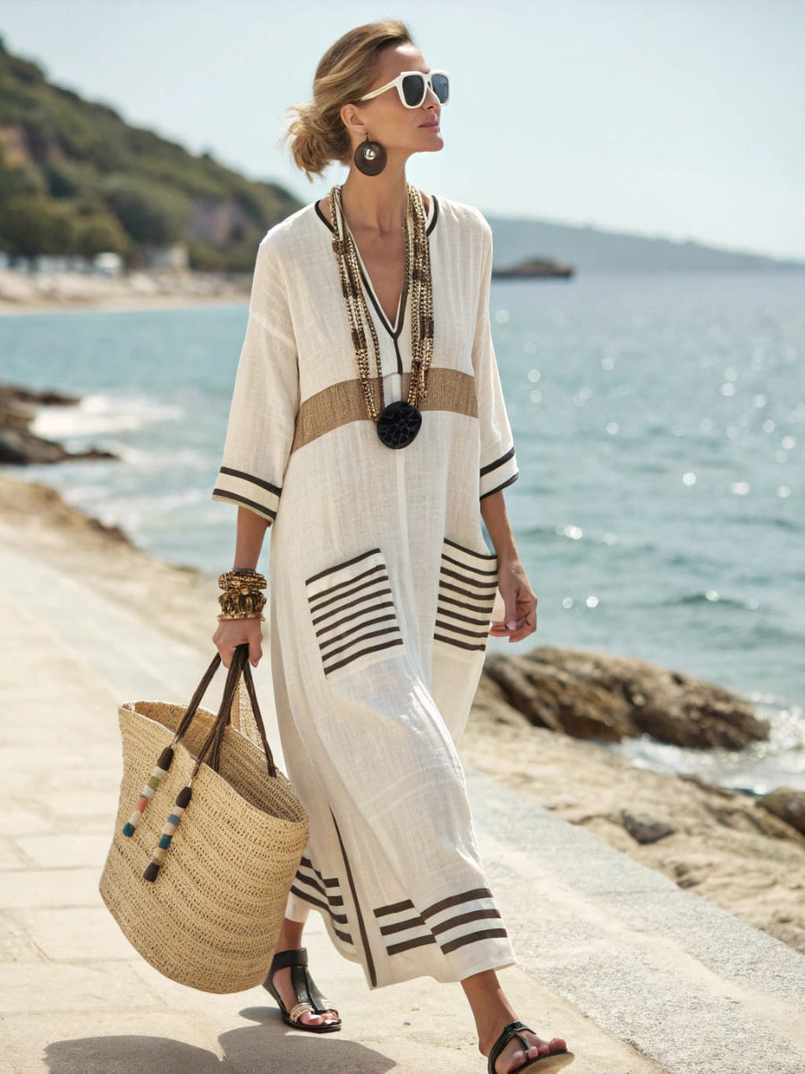 Woman in a white dress with black stripes standing on a beach.