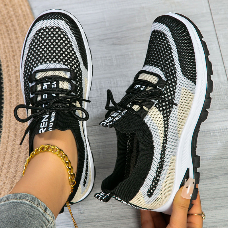Black and white sneakers worn on a gray floor with a gold bracelet visible.