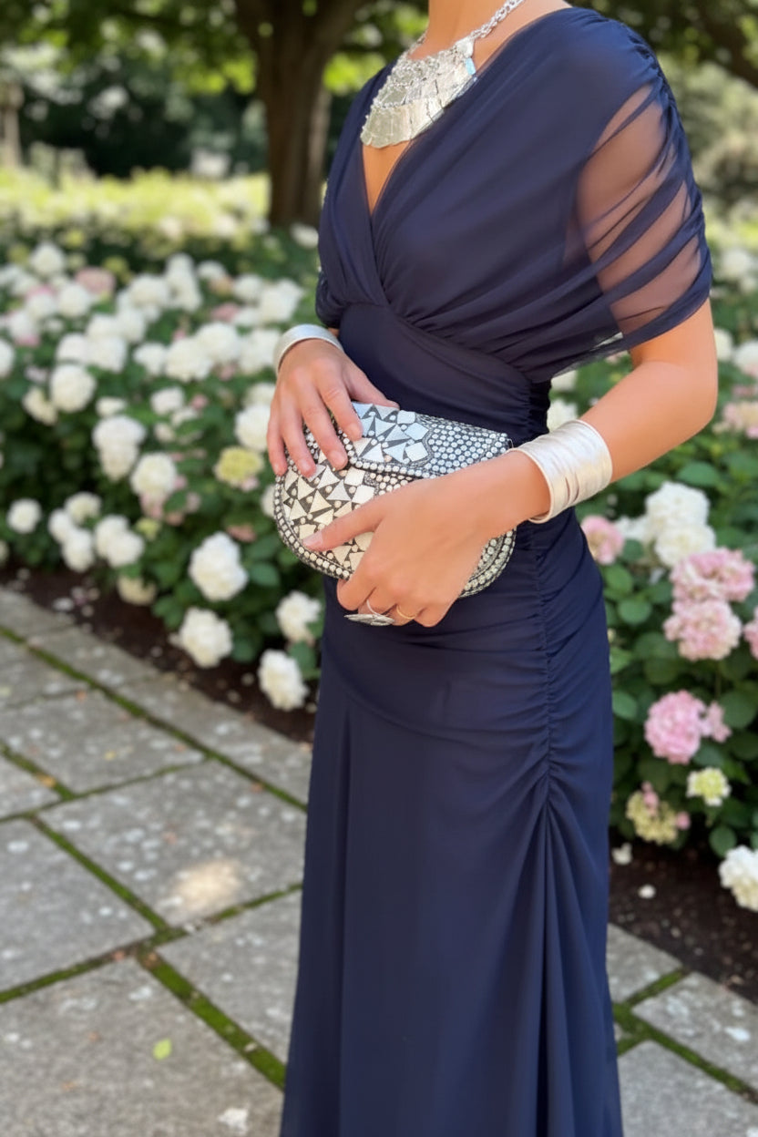 Navy blue dress with sheer sleeves and silver clutch held by a hand.