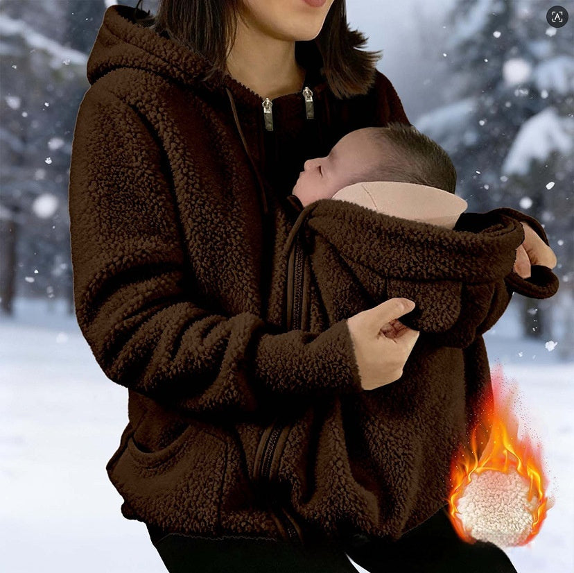 A woman in a brown sherpa fleece hooded jacket holds a baby in a matching baby carrier pouch. The background is a snowy outdoor scene, and a graphic of a fireball with a thermometer appears in the bottom right corner to illustrate the warm interior.