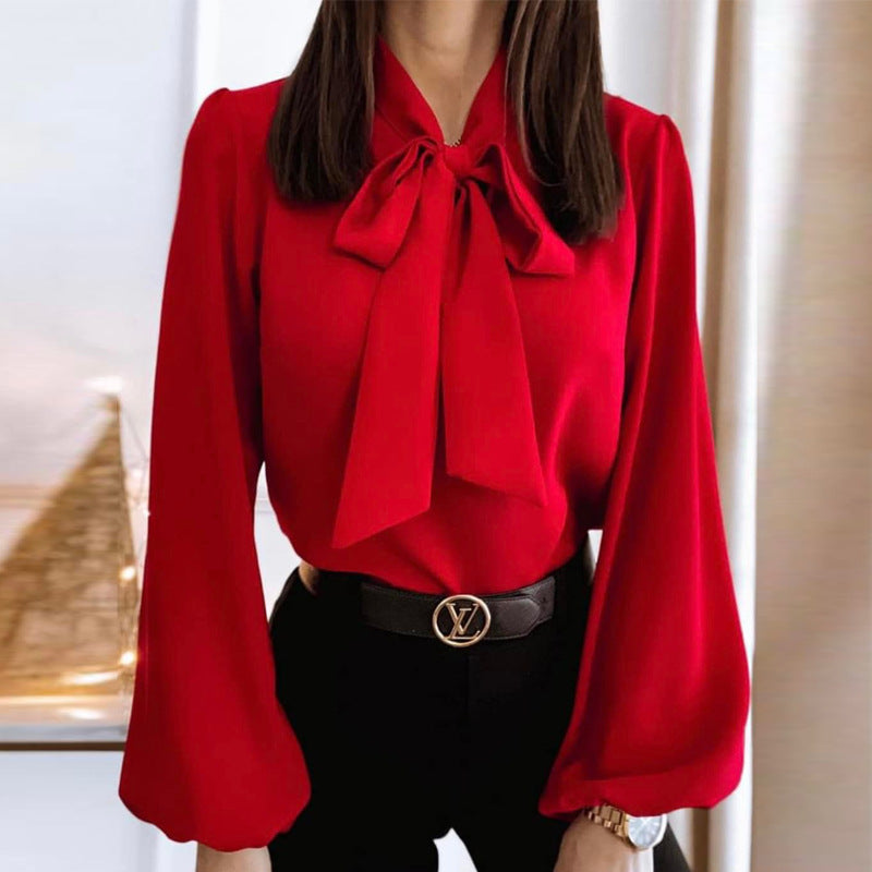 Red blouse with a large bow and black pants worn by a person indoors.