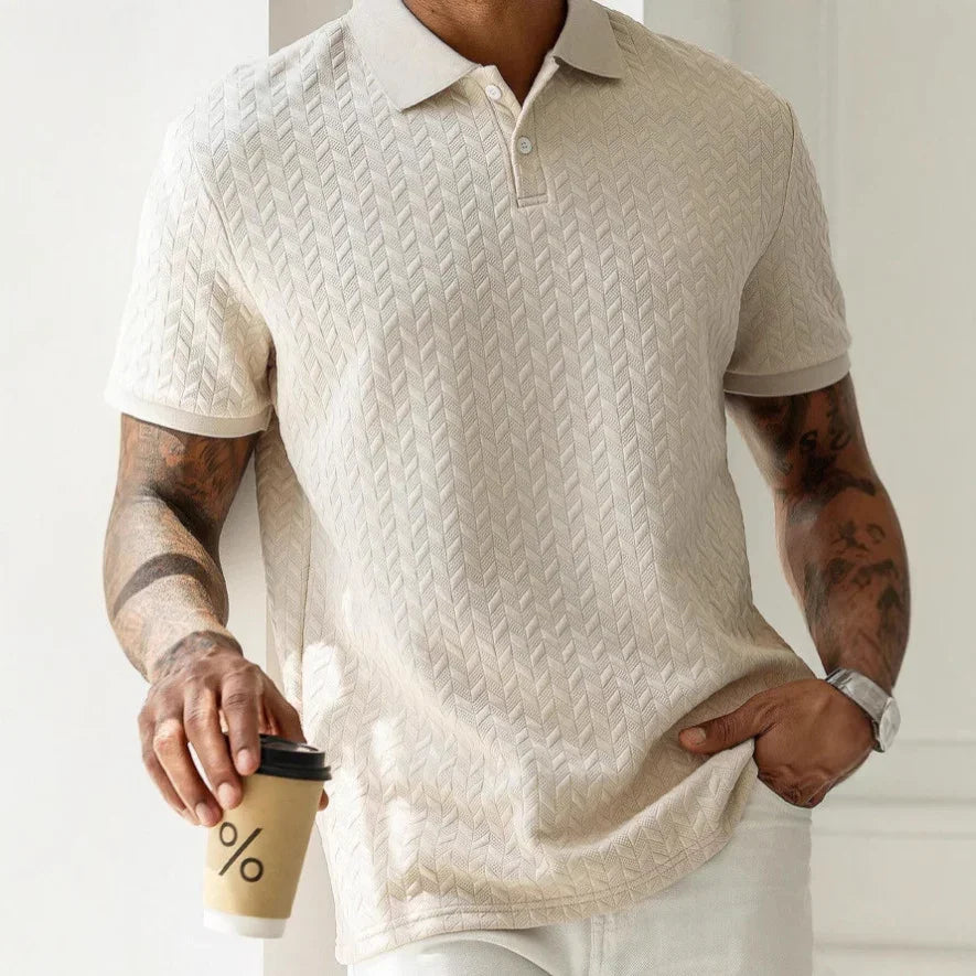 Man wearing a beige patterned polo shirt holding a coffee cup.