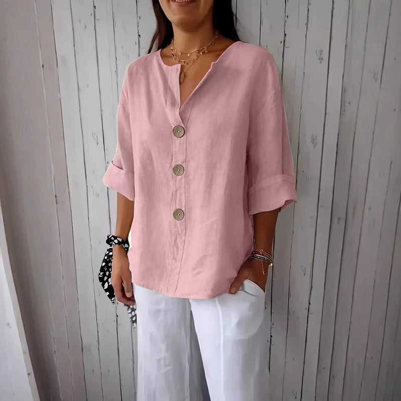 Person wearing a pink button-up shirt and white pants against a wooden background
