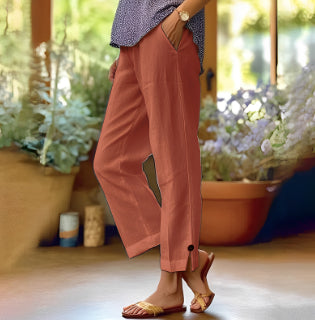 Person wearing pink pants and sandals in a home setting with plants.