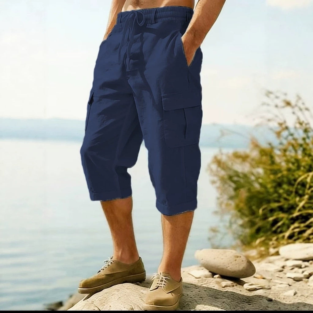 A person wearing navy blue drawstring cargo shorts with side pockets, standing on rocks by a lake with water and distant land visible in the background.