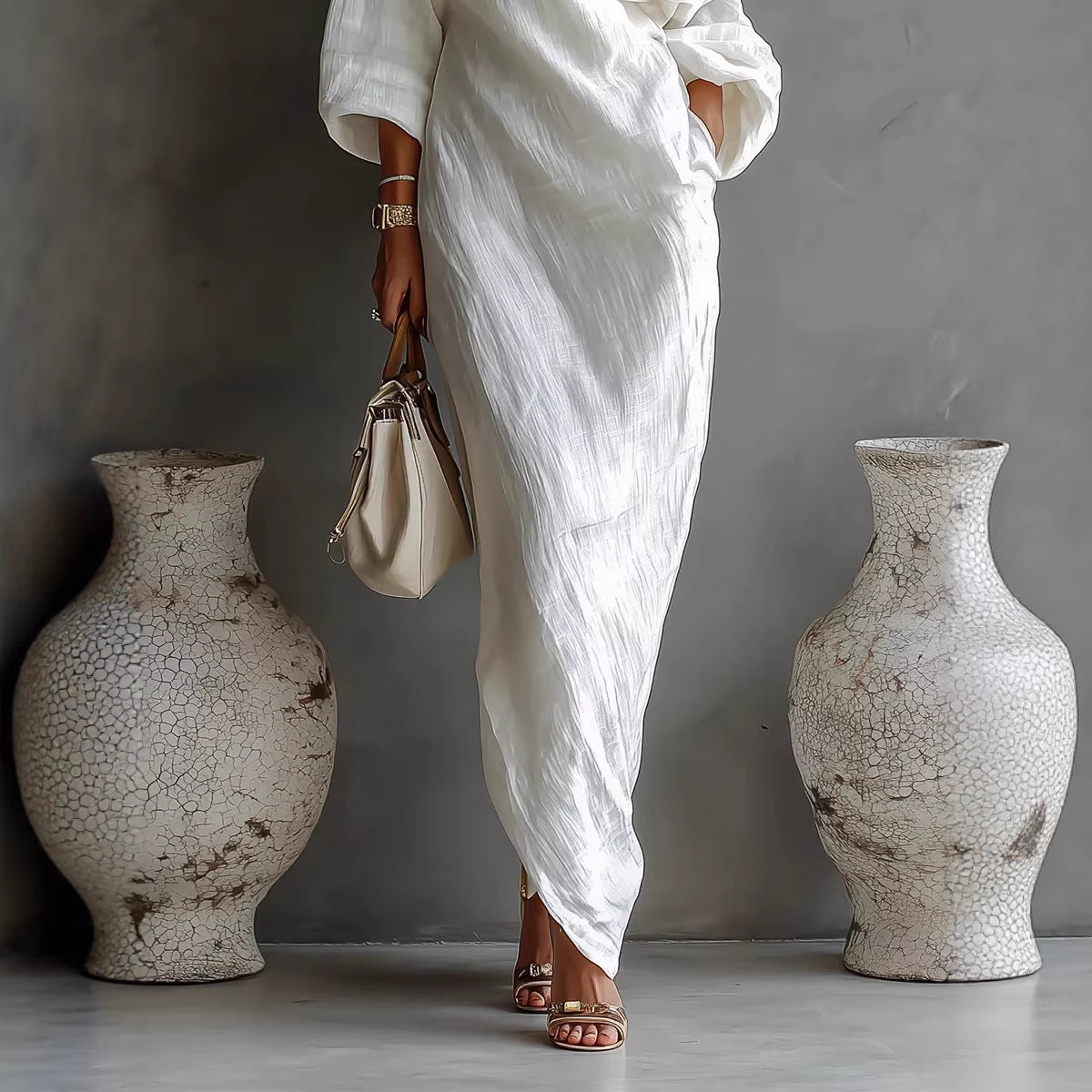 Person in a white dress standing between two large, textured vases against a gray background.