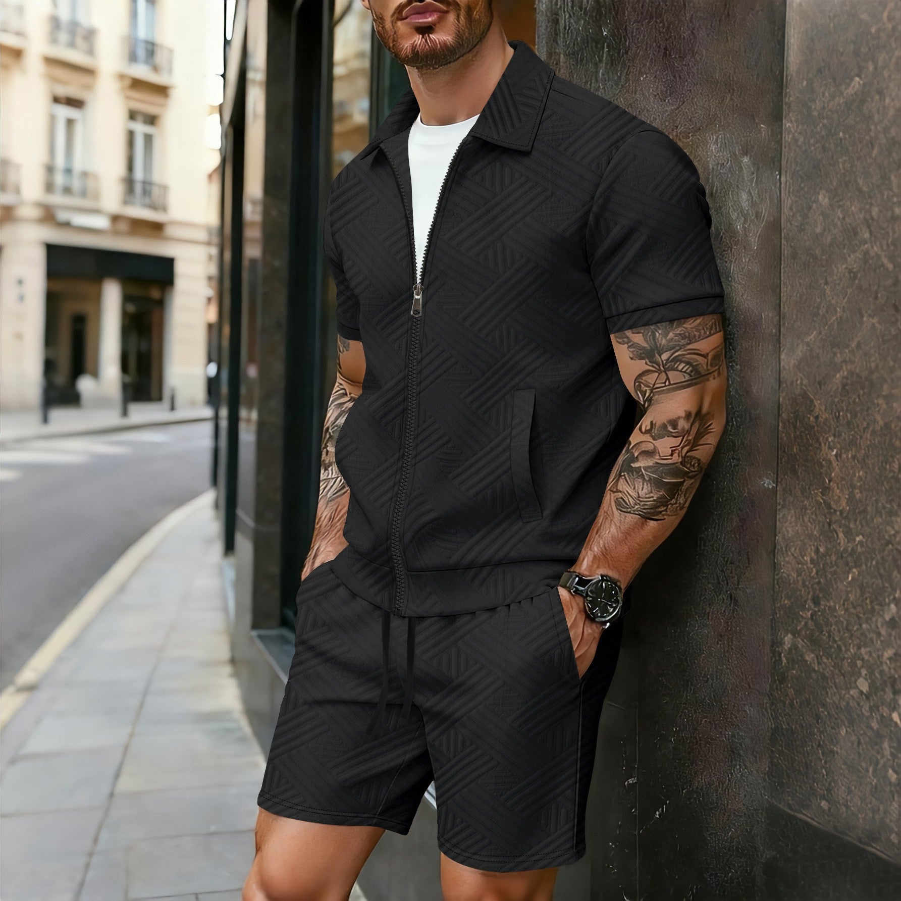 Man wearing a black outfit leaning against a wall in an urban setting