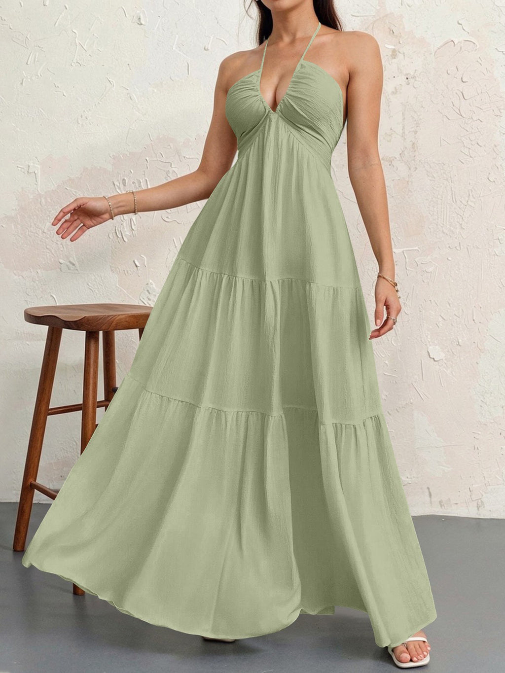 Woman wearing a green halter neck dress against a white brick wall.