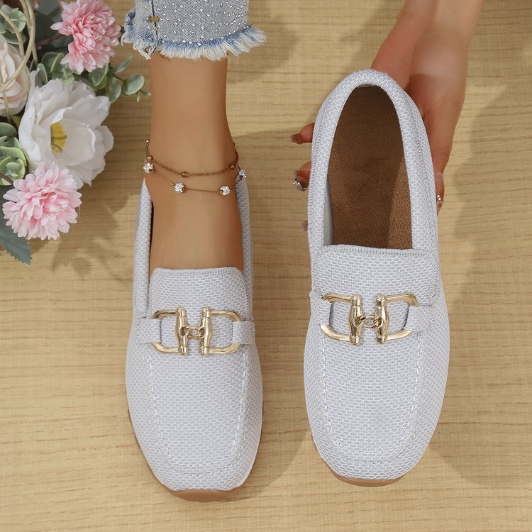 White loafers with gold buckles on a wooden floor with flowers in the background