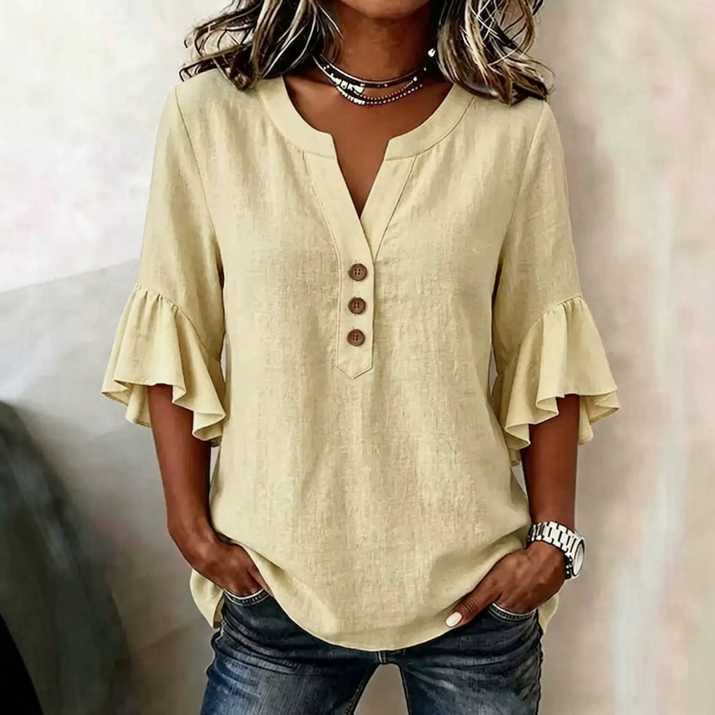 Woman wearing a beige blouse with ruffled sleeves and blue jeans against a neutral background