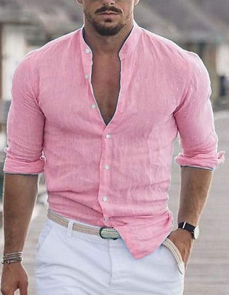 Man wearing a pink shirt with rolled-up sleeves and white pants outdoors.