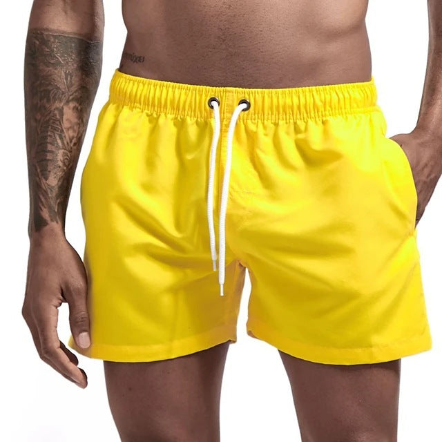 Yellow swim shorts with a white drawstring on a neutral background