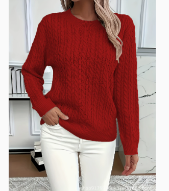 A woman wearing a red cable-knit crewneck sweater and white pants, standing in front of a white paneled wall.