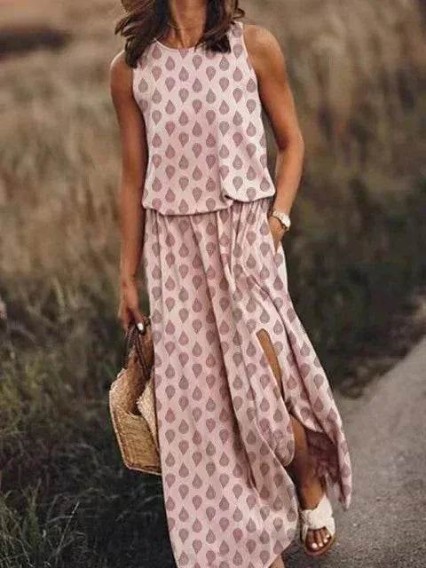 Woman wearing a pink patterned maxi dress with side slit, holding a straw bag outdoors
