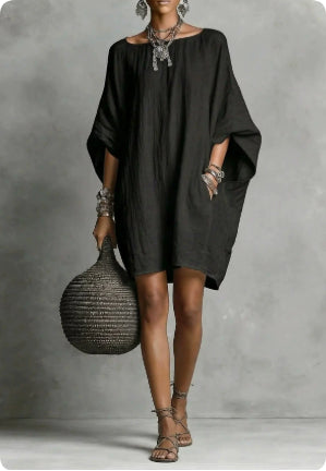Woman wearing a black dress holding a woven bag against a gray background