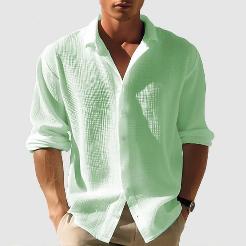 Person wearing a light green button-up shirt with rolled-up sleeves on a plain background