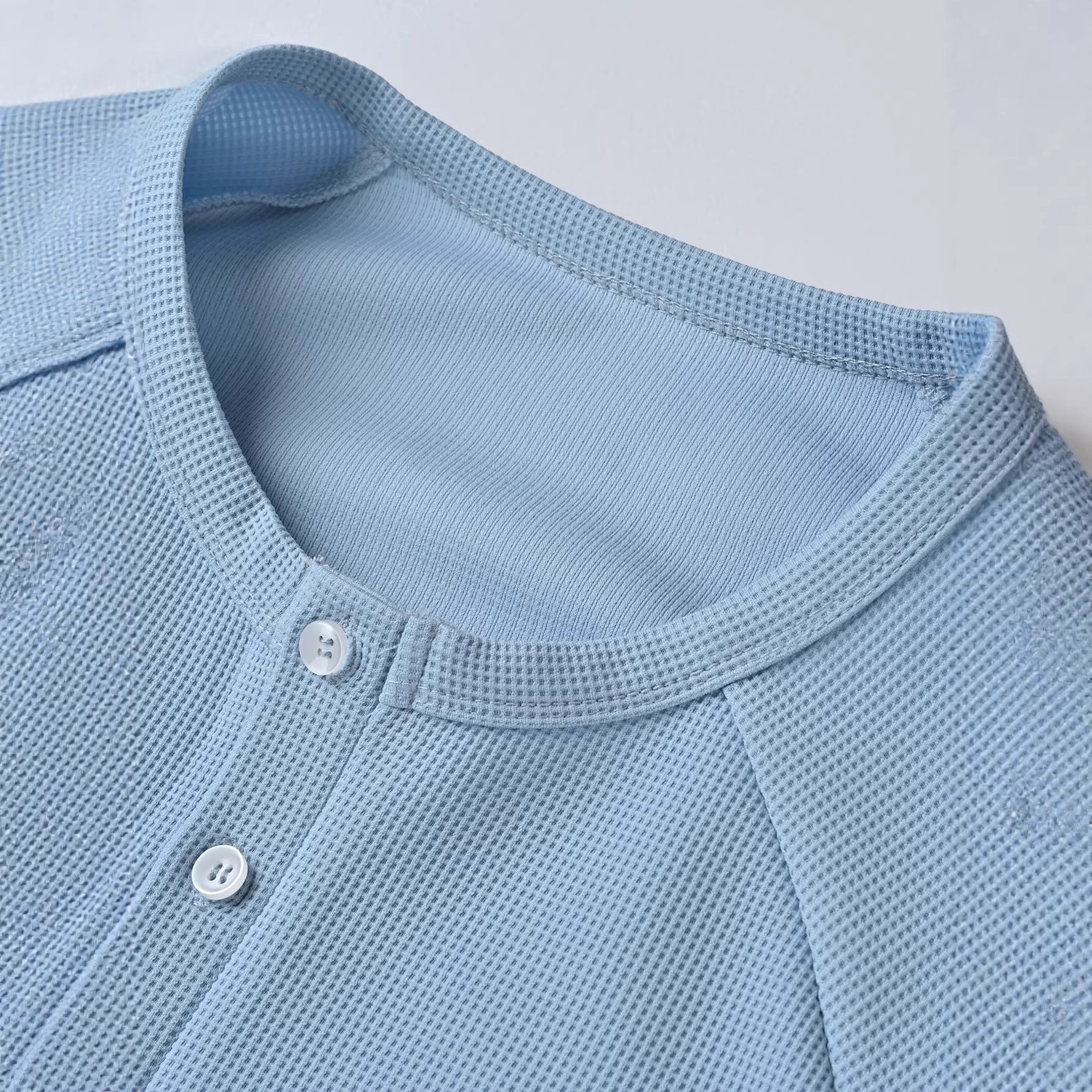 Close-up of a light blue textured shirt with buttons on a white background