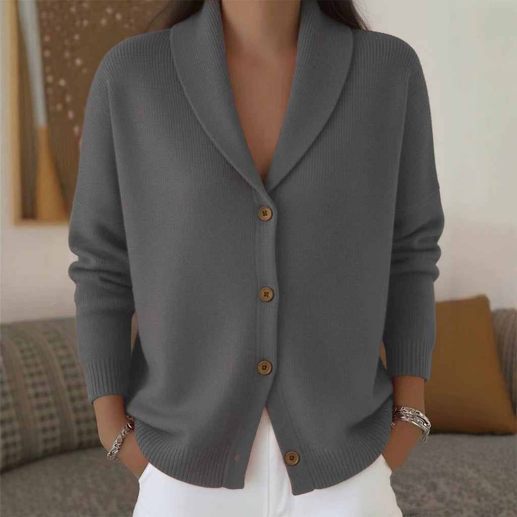 Person wearing a gray cardigan with brown buttons in a blurred indoor setting