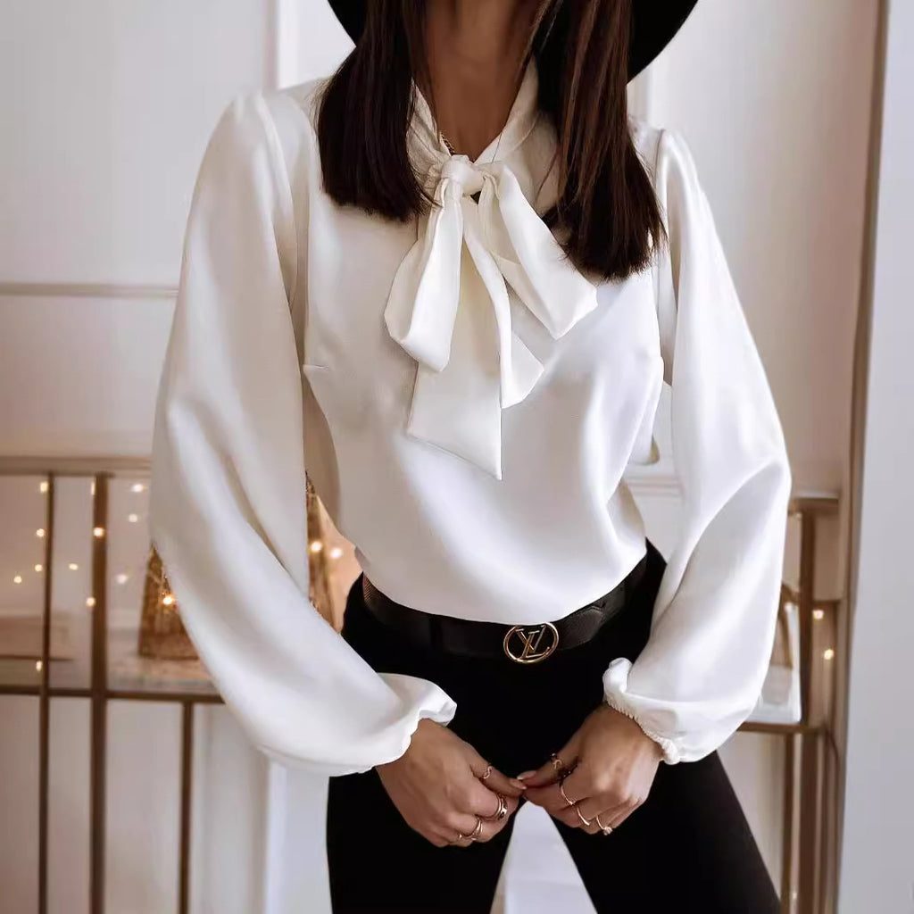White blouse with a bow tie worn by a person, with a blurred indoor background.