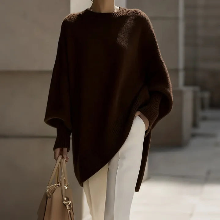 Person wearing a brown poncho and holding a beige handbag in an urban setting.