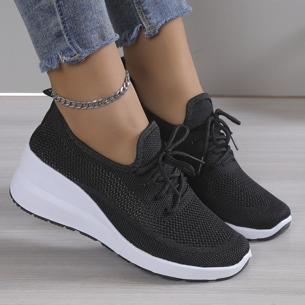 Black sneakers with white soles worn with light blue jeans on a neutral background