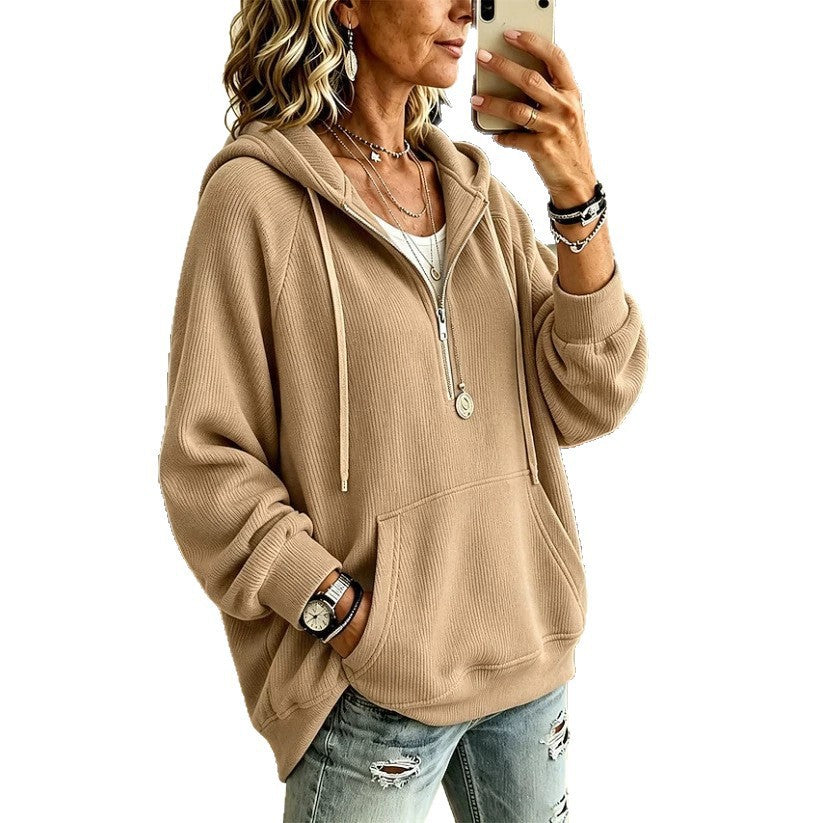 A woman takes a mirror selfie wearing a beige ribbed half-zip hoodie with a drawstring hood and front kangaroo pocket, paired with distressed blue jeans.