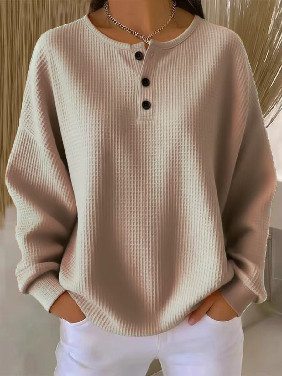 A woman wearing a beige waffle-knit long-sleeve henley sweater with three black buttons, paired with white pants.