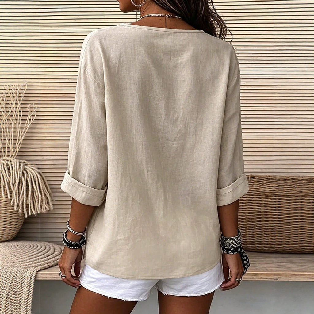Person wearing a beige long-sleeve shirt and white shorts against a wooden panel background